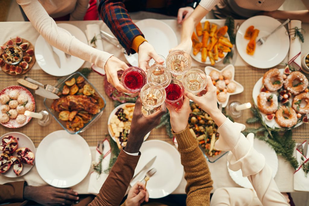 A group of people clinking their drinks in cheers at a festive gathering over a Christmas dinner