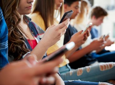 Stock image of multiple teens staring at their phones