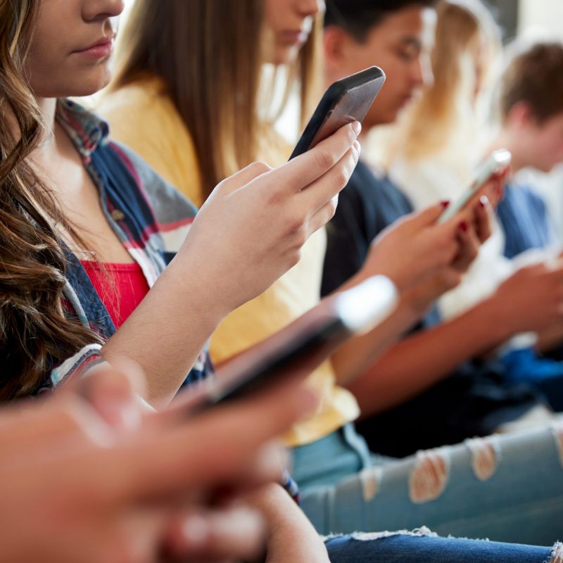 Stock image of multiple teens staring at their phones